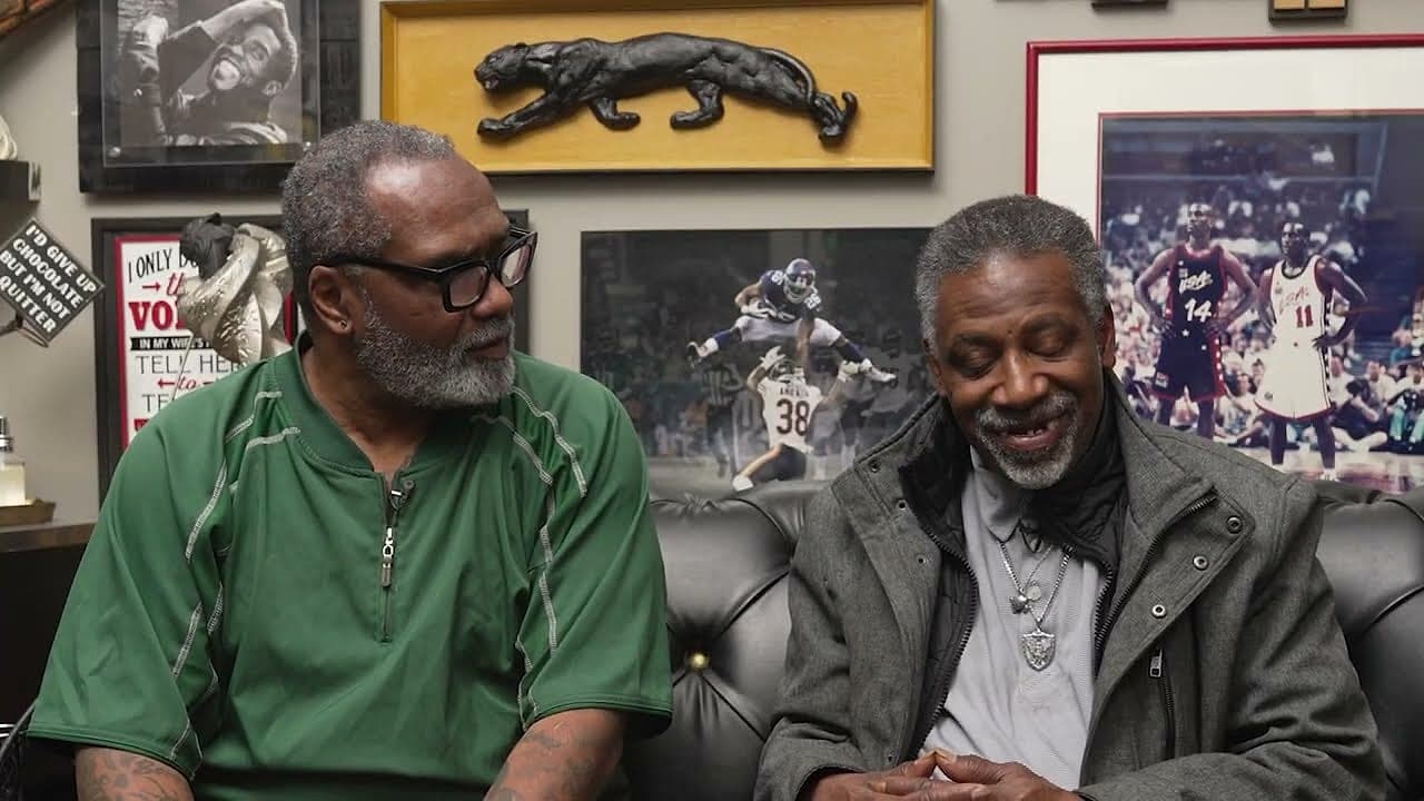 Two old friends smiling side by side on the barbershop couch